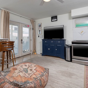 The living area features a large TV, stylish blue cabinetry, and a comfortable seating area leading to a lovely outdoor view