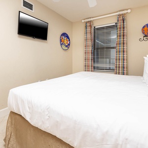 This guest bedroom features a king bed, a flat-screen TV, and colorful curtains that add a cheerful touch