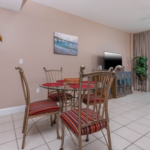 This inviting living area features a glass dining table, colorful striped chairs, and a TV, with a beautiful beachfront view