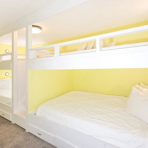 Bright yellow walls frame cozy bunk beds with soft linens, creating a cheerful space perfect for family or group stays