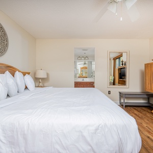 Spacious master suite features a plush king bed, a wooden dresser, and a mirror reflecting the adjoining bathroom