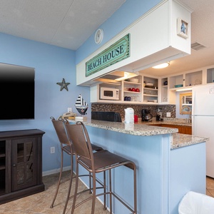 This inviting kitchen features granite countertops and a seating area below a beach house sign for enjoying meals together