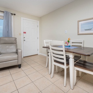This inviting dining area features a table for four, a cozy armchair, and a serene lagoon view through large windows