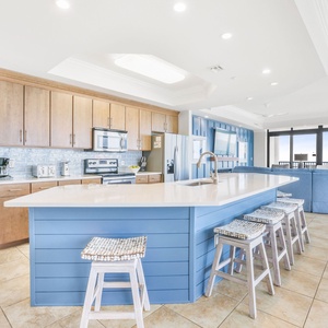 The kitchen features sleek modern appliances, a spacious blue island with seating, and a costal vibe to compliment your stay