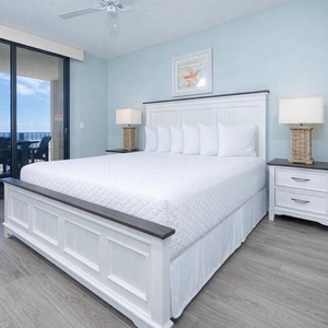 Spacious master featuring a king bed, light blue walls, and access to the balcony with seating for enjoying the beach view