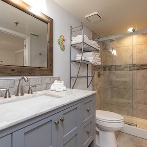 The bathroom features a stylish marbled countertop, a glass-enclosed walk-in shower, and neatly arranged towels on a rack