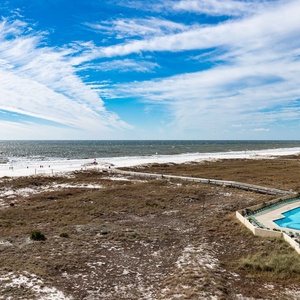 Stunning beah view with white sand, gentle waves, and a pool area surrounded by lush greenery and lounge chairs