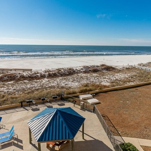 The view showcases a serene beach with white sand, framed by a pool area and a shaded gazebo for relaxation