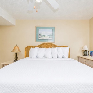 A cozy bedroom features a large king bed with plush white bedding, a wicker headboard, and a charming dresser with a mirror