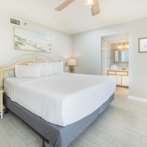 Master bedroom featuring a king bed with plush pillows, a cozy armchair, and elegant coastal decor