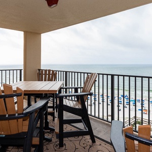 A spacious balcony features a table and chairs, offering a serene view of the beach and the gentle waves below