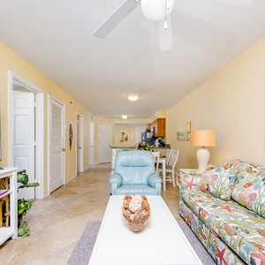 This inviting living area features a colorful floral couch, a large TV, and a view leading to the kitchen space