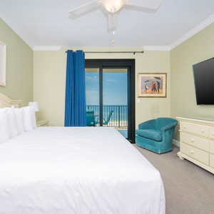 Master suite bedroom featuring a king bed, a teal accent chair, and balcony access with a view of the beach