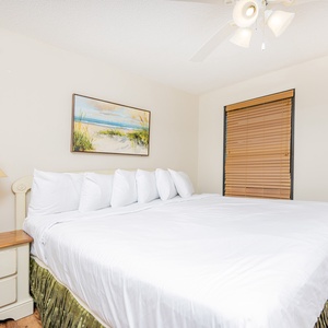 Brightly lit guest bedroom featuring a large king bed with crisp white linens, a bedside lamp, and a beach painting above