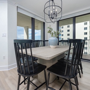 Dining area features a large table surrounded by black chairs, with views of the beach visible through expansive windows