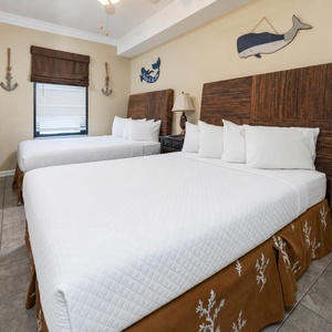 This guest bedroom features two double beds with textured headboards, a TV, and nautical decor, creating a relaxed beach vibe