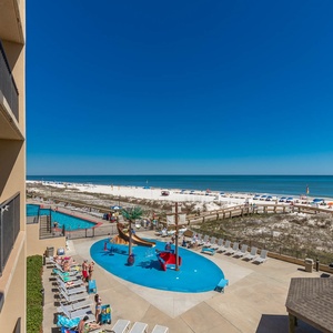 A vibrant pool area with a splash park overlooks the beach, inviting relaxation under the clear blue sky