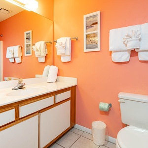 Brightly colored guest bathroom featuring a large mirror, white towels, and a tub/shower combo against a coral backdrop
