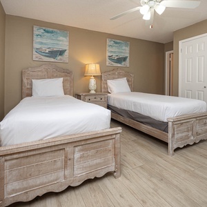 The guest bedroom features two twin beds with rustic wooden frames, soft lighting, and beach artwork for a relaxed atmosphere