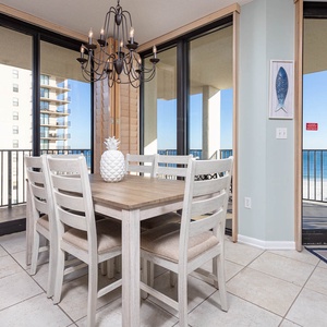Dining area features a wooden table with seating for six, complemented by a beach view through expansive glass doors