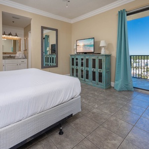 Brightly decorated master suite features a king bed, a teal accent cabinet, and a seating area with a view of the outdoors