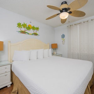 The master bedroom features a comfortable king bed, a TV, and bright decor with a tropical theme, perfect for relaxation