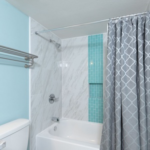 The guest bath features a tub/shower combo with a stylish gray and turquoise color scheme, complemented by modern tile