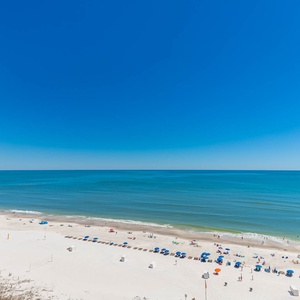 A serene beach view showcases white sand and colorful umbrellas, inviting relaxation under a clear blue sky