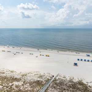 Expansive view of a serene beachfront with colorful umbrellas and sun loungers set against soft white sand and gentle waves
