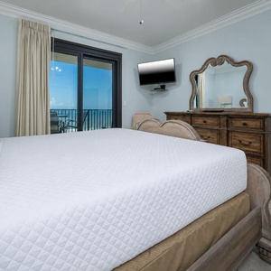 Master suite featuring a king bed, elegant wooden dresser, and a balcony view of the beach through sliding glass doors