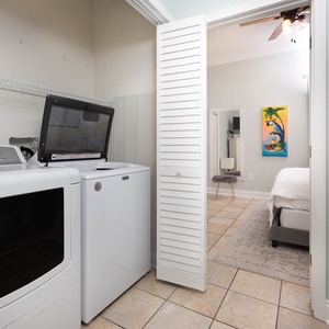 Laundry area featuring a washer and dryer, with a glimpse of a colorful tropical artwork and a cozy guest bedroom beyond