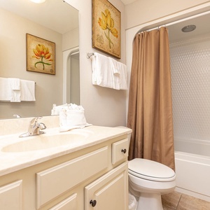 This guest bathroom features a light-colored vanity, a relaxing shower with a curtain, and decorative floral art