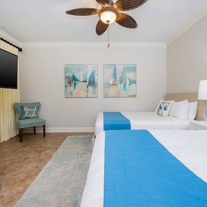 Rest in the guest room featuring two queen beds, coastal decor, and a cozy chair inviting you to relax and unwind