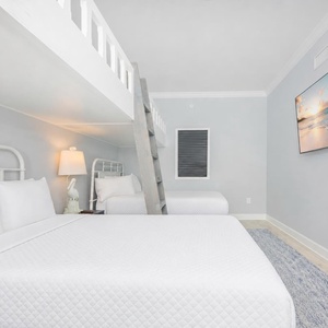 Cozy bunk room with two lofted twin beds above two queens and soft lighting