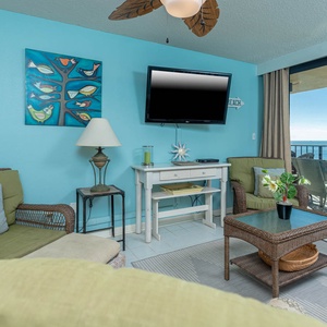 The inviting living area features a large TV, cozy seating, queen sofa-sleeper, and a beautiful view of the beach