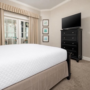 The master bedroom features a large king bed, a TV for entertainment, and views through glass doors leading to a dining area