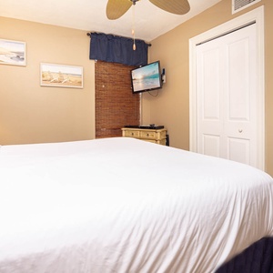 Cozy bedroom featuring a plush king bed, bedside lamp, wall-mounted TV, and warm-toned decor for a relaxing retreat