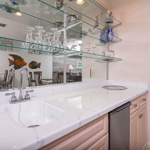 Fix a drink at this stylish wet bar area with a spacious countertop, ice maker, and beautiful glassware on display
