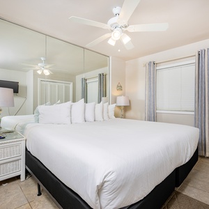 This guest bedroom features a large bed with plush pillows, a TV for entertainment, and soft lighting from the ceiling fan