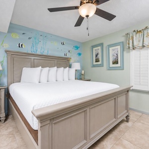 Serene bedroom features a king bed with white linens, beach wall art, and light green accents for a tranquil vibe