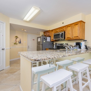 This kitchen features granite countertops, wooden cabinetry, and a breakfast bar with white stools, perfect for casual dining