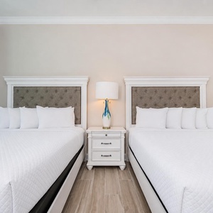 Inviting guest bedroom featuring two comfortable queen beds, soft linens, and a stylish lamp