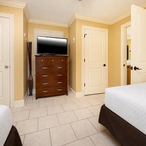 Guest room featuring two double beds, a wooden dresser with a TV, and a warm, inviting color scheme