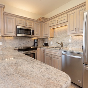 Light wood cabinetry complements the granite countertops in this kitchen, featuring a coffee maker and stainless appliances
