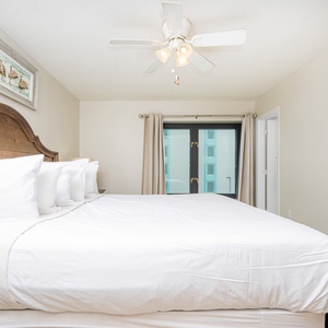 This bedroom features a cozy king-sized bed with white linens and a view of the nearby balcony through large windows