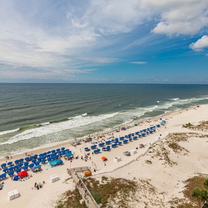 The stunning balcony view showcases vibrant blue umbrellas lining the sandy shore, perfect for a relaxing day by the water