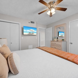Comfortable guest bedroom featuring a queen bed with decorative pillows, a TV, and a dresser with a mirror