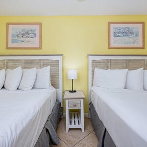 Two neatly made double beds with plush white pillows, accented by a small nightstand and artwork