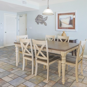 Dining area features a wooden table surrounded by six chairs, accented by coastal artwork and a light blue wall