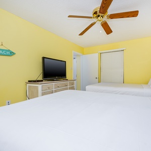 Bright yellow walls complement two full beds and a TV on a dresser, creating a cheerful and inviting guest room